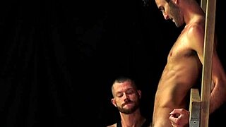 A dominant older tilts his head down, a muscular young man in bondage serves a dominant older partner gay BDSM dreamboybondage