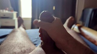 Intensely masturbating a massive cock in the bedroom with sunlight streaming through.