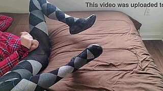 A shemale is jerking off while wearing a plaid dress and argyle tights.