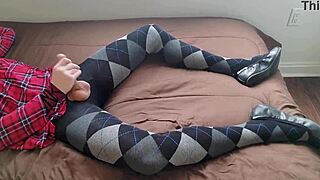 A shemale is jerking off while wearing a plaid dress and argyle tights.