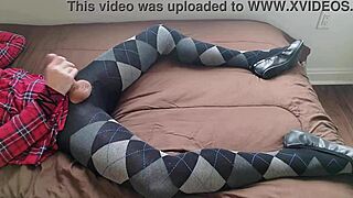 A shemale is jerking off while wearing a plaid dress and argyle tights.